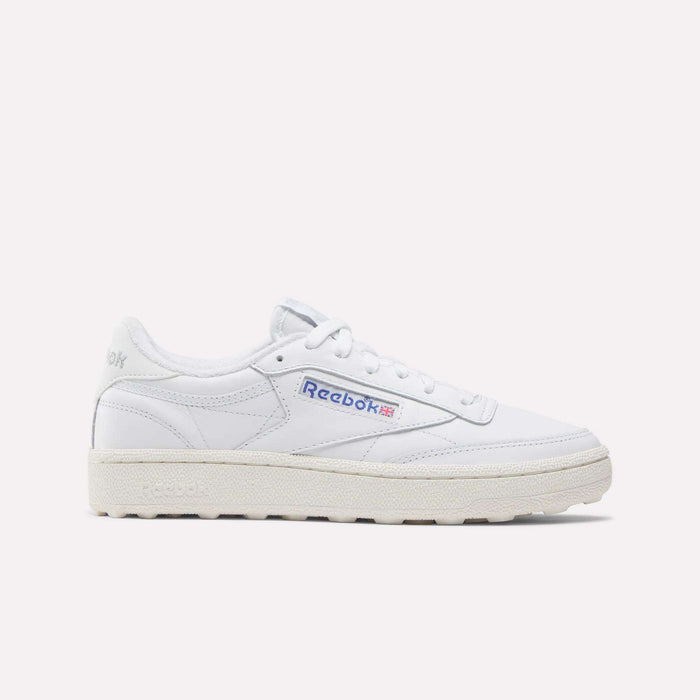 The Reebok Women’s Club C Golf Shoes feature a white upper, cream sole, blue and red side logo, spikeless outsole, and white laces, shown against a plain white background.