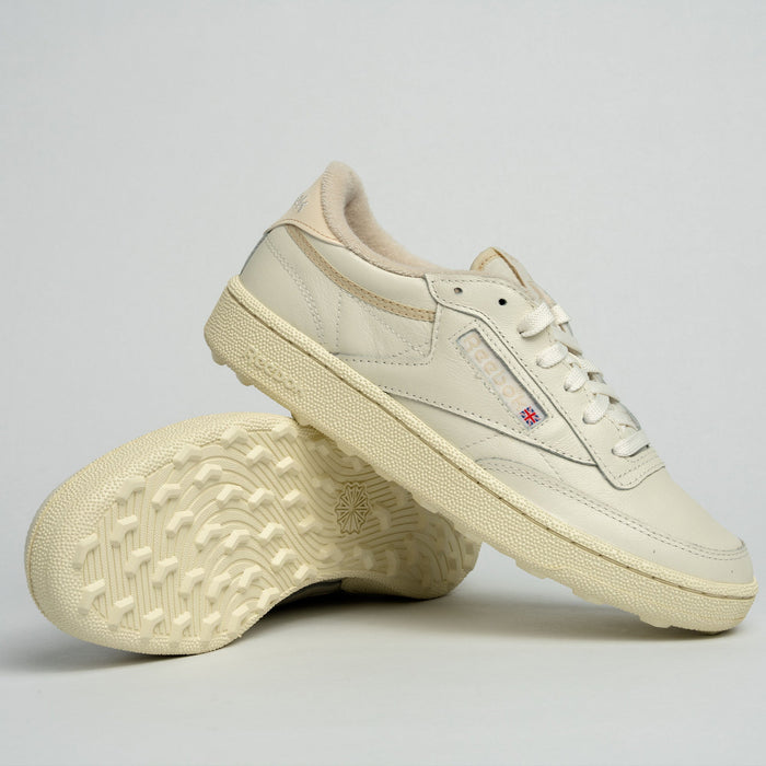 A pair of off-white Reebok Women's Club C Golf Shoes, crafted with water-resistant leather—one upright, the other tilted to show its textured sole—are displayed against a simple light grey background.