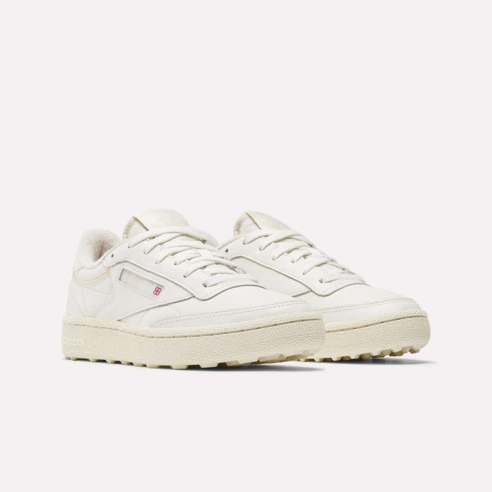The Reebok Women's Club C Golf Shoes feature off-white water-resistant leather, textured rubber soles, white laces, subtle stitching, a spikeless design, and a small red and blue logo on the side.