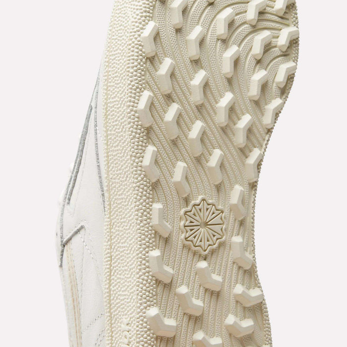 Close-up of the white sole on Reebok Women's Club C Golf Shoes, highlighting its textured tread and central star-like design as the shoe is positioned with the sole facing the camera.
