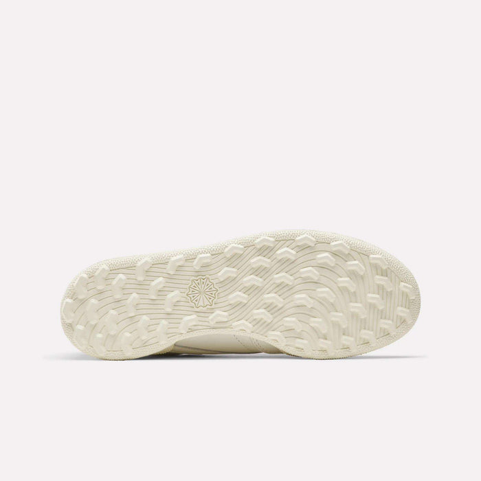 The sole of the Women's Club C Golf Shoes by Reebok features a beige, spikeless design with a textured wavy tread and a star emblem in the center, displayed against a plain white background.