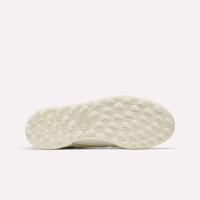 The sole of the Women's Club C Golf Shoes by Reebok features a beige, spikeless design with a textured wavy tread and a star emblem in the center, displayed against a plain white background.