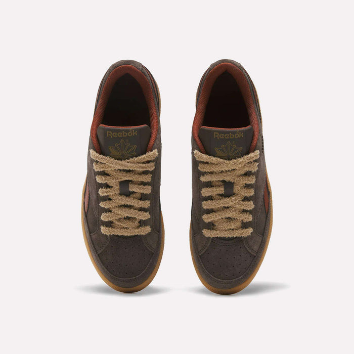 A pair of Reebok Women’s Club C Grounds 70 Shoes is shown from above against a plain white background. Featuring brown suede uppers, tan textured laces, gum soles, and a reddish-brown inner lining, these retro sneakers blend classic style with modern comfort.