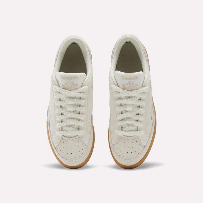 A pair of Reebok Women’s Club C Grounds 70 Shoes in cream, featuring gum soles, is displayed from above against a light background. These retro sneakers offer textured side panels, a suede upper, and classic Reebok branding on the tongue.