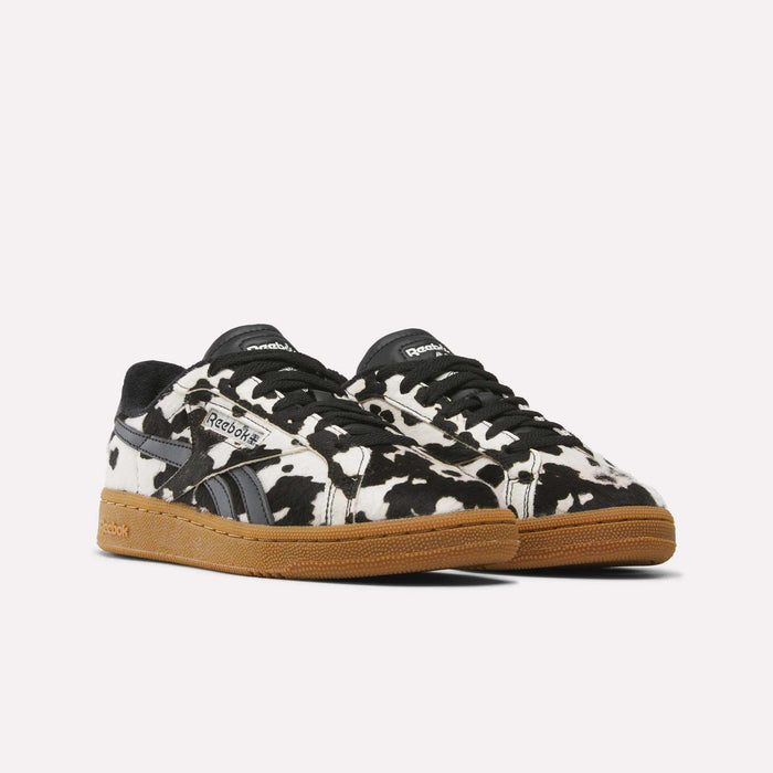 A pair of Women’s Club C Grounds UK 1.0 Shoes by Reebok in a bold black and white cow print with brown rubber soles, positioned slightly angled to the right against a plain white background. These animal print sneakers bring an eye-catching update to the Reebok collection for women.
