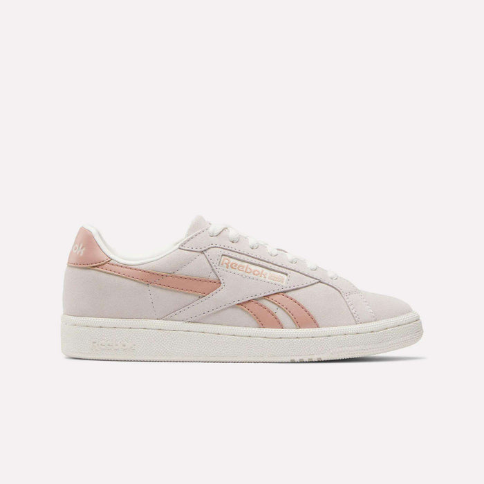 The Reebok Women's Club C Grounds UK Shoes feature a light pink and white suede and leather finish with the Reebok logo and a pink stripe on the side, displayed against a plain white background.