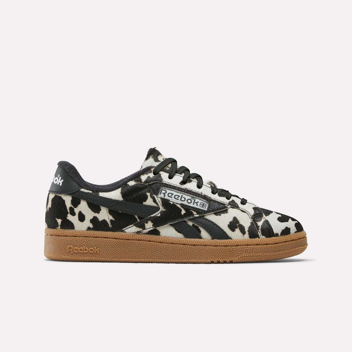 The Reebok Women's Club C Grounds UK Shoes feature a bold black and white cow print upper, black laces, logo accents, and a brown gum sole—making them a standout choice for women’s sneaker collections.