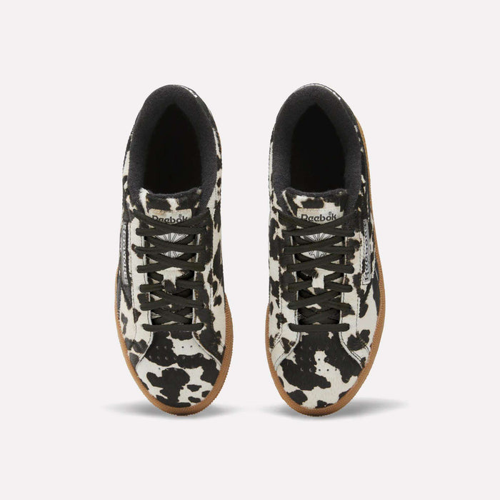 Top view of Reebok Women's Club C Grounds UK Shoes with black and white cow print uppers, black laces, black inner lining, white midsoles, and tan rubber outsoles on a plain white background.