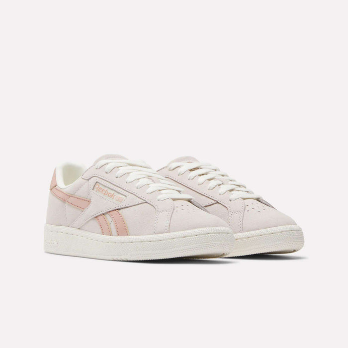 The Women's Club C Grounds UK Shoes by Reebok are light pink with white soles and laces, featuring pink Reebok stripes and branding on the side and tongue. Made from suede and leather, they're shown against a plain white background.