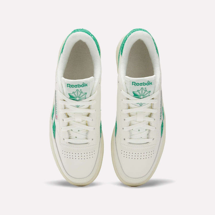 Top view of a pair of Reebok Women’s Club C Revenge Shoes in white with green accents and a green leaf logo on the tongue, placed side by side on a plain white background.