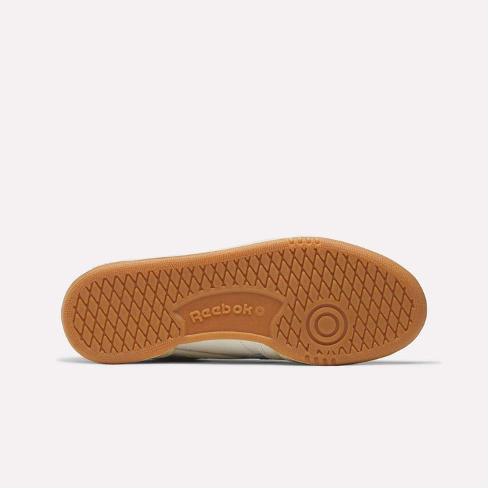 The image displays the gum-colored sole of Reebok Women's Club C Revenge Shoes, highlighting the Reebok logo, a circular toe pattern, and diamond-textured tread for grip. This popular women's court shoe is shown against a plain white background.