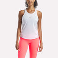 A woman stands facing forward against a plain background, wearing a white Reebok Women's Core Tank Top with moisture-wicking fabric and a small chest logo, paired with bright pink leggings.
