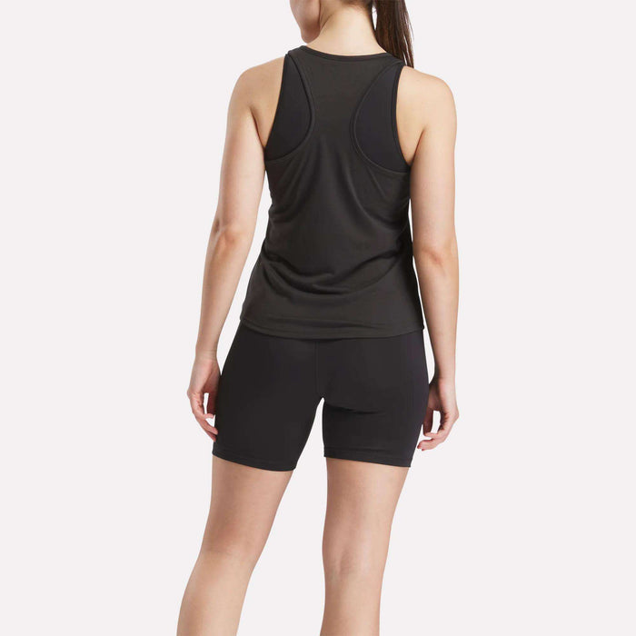 A woman faces away, wearing a Reebok Women's Core Tank Top and black sweat-wicking shorts against a plain light background.