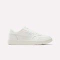 A women’s low-top sneaker in Chalk/Dew/White, crafted from full grain leather with subtle stitching, perforations, and a textured sole, displayed on a plain light background and shown from the side. These Reebok Women’s Court LXS Shoes embody the refined style of classic court footwear.