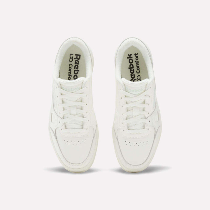 Two white Reebok Women’s Court LXS Shoes are viewed from above on a plain, light background. Reebok and LJ Comfort are visible on the insoles in black text. These women’s court shoes feature full grain leather, white laces, and a classic, simple design.