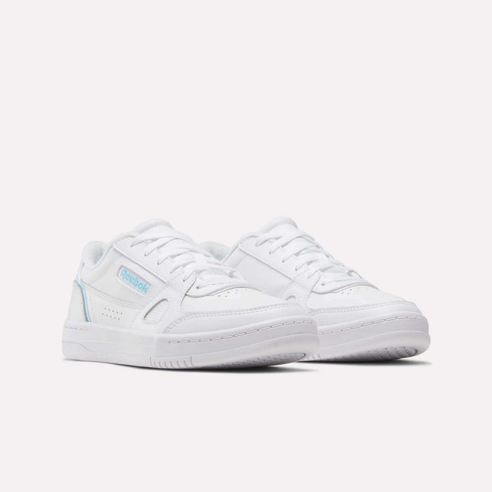 A pair of white Reebok Women’s Court LXS Shoes with light blue accents, crafted from premium full grain leather, displayed on a plain white background and positioned at a slight angle to showcase the side and front of these classic women’s court shoes.