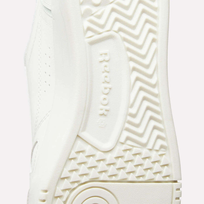 Close-up of the sole of a white Reebok Women’s Court LXS Shoe, featuring the brand name and textured patterns such as zigzags, small triangles, and circular designs. Crafted from premium full grain leather, these women’s court shoes blend classic style with durable comfort.