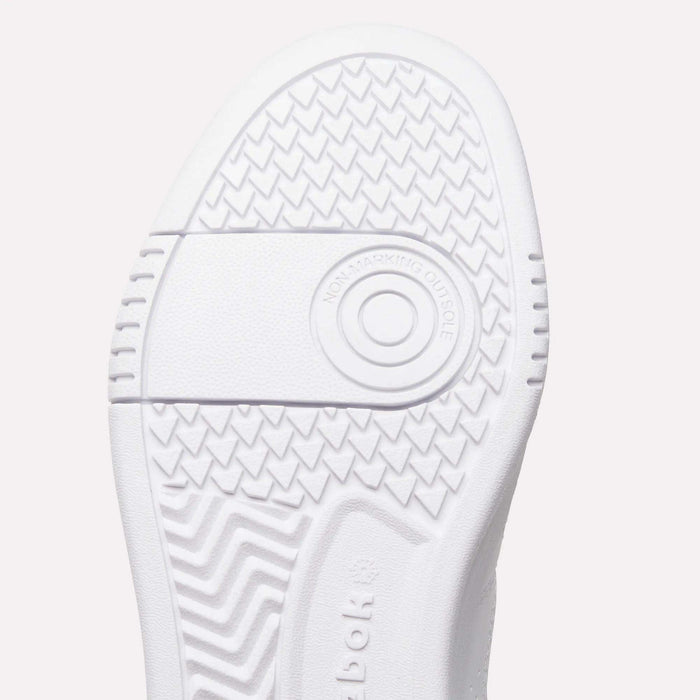Close-up of the white sole of Reebok Women’s Court LXS Shoes, a premium choice in women’s court shoes, featuring zigzag and circular tread patterns. Crafted with full grain leather, the words NON-MARKING OUTSOLE are visible inside a ring near the center.