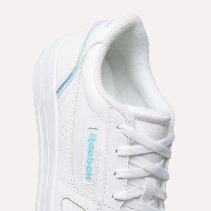 Close-up of the Women’s Court LXS Shoes by Reebok, crafted from white full grain leather with light blue accents, white laces, and visible Reebok branding on the side and tongue, set against a light background.