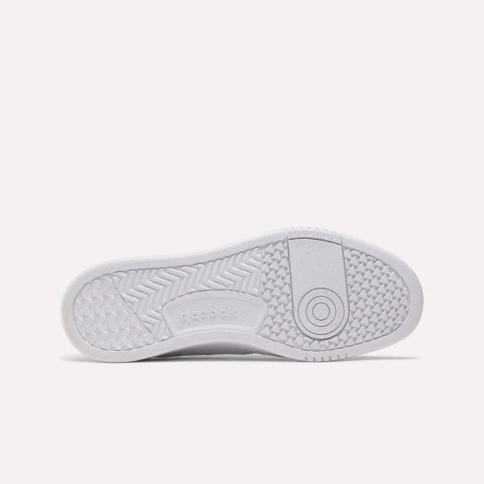 The image shows the white rubber sole of a Reebok Women’s Court LXS Shoe viewed from below, featuring various textured patterns and the Reebok logo in the center—a stylish choice among women’s court shoes crafted with premium full grain leather for durability and comfort.