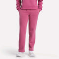 Visible from the shoulders down, a person models Reebok Women's Cozy Classic Sweatpants in bright pink with a matching sweatshirt and white sneakers, standing hands-in-pockets against a plain white background.