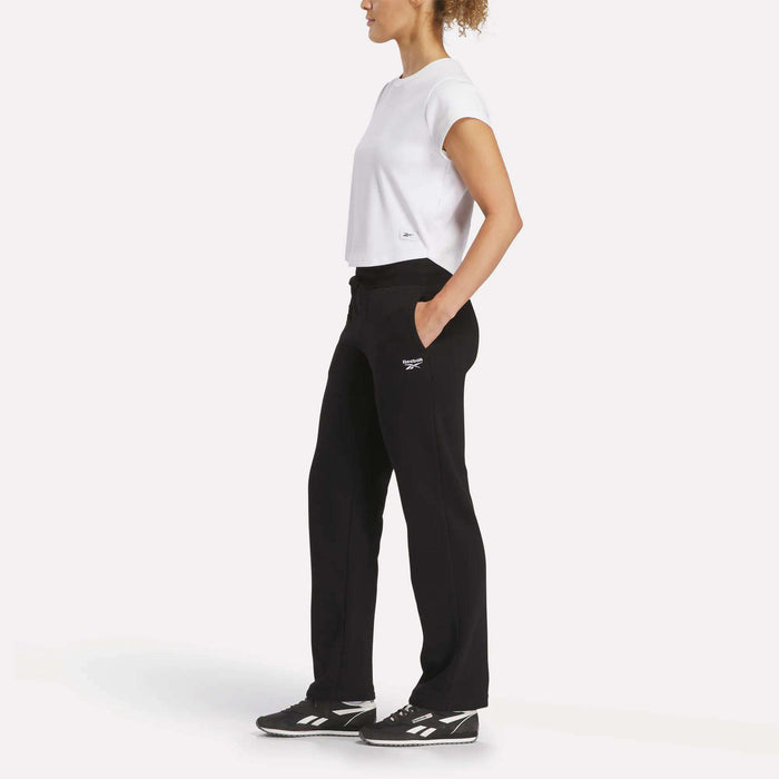 A woman in a white shirt and black pants, styled with Reebok Women's Cozy Classic Sweatpants made from a soft cotton blend.