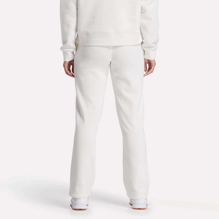 A person is seen from behind, showing only lower back and legs, wearing Reebok Women's Cozy Classic Sweatpants in soft white cotton blend with a matching long-sleeve top and white shoes, set against a plain white background.