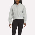 A person wears a Reebok Women's Cropped Full-Zip Hoodie in Grey Heather, featuring front pockets, paired with black leggings against a plain light background.