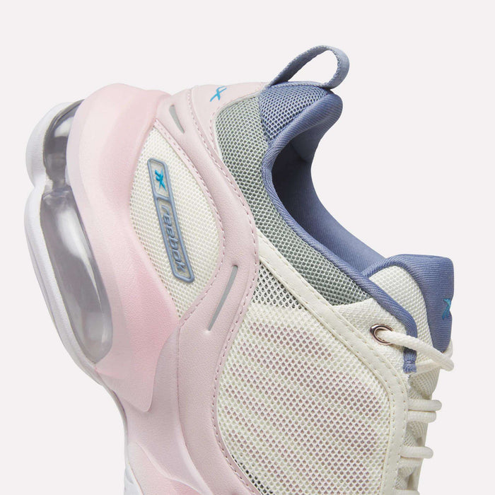 A close-up of the Reebok Women's DMX Series 3000 Training Shoes in white, highlighted with light pink and blue accents, showcases a mesh upper, blue laces, and a visible air cushion in the heel—demonstrating Reebok’s innovative DMX 3 Technology that distinguishes these shoes as among the best cushioned options for all-day comfort.