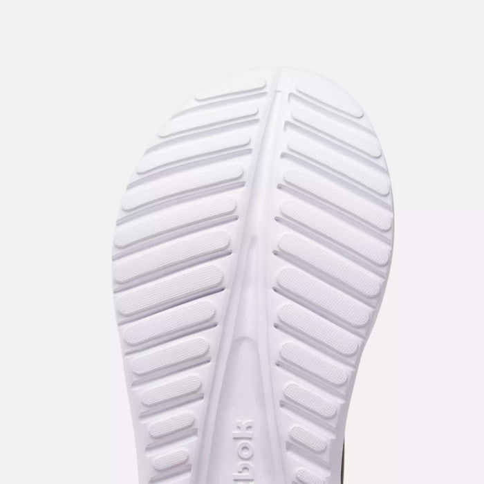 Close-up of the sole of a white Reebok Women's Energen Lux Running Shoe, featuring horizontal and diagonal grooves for traction. The lightweight, ribbed sole has a textured pattern with the Reebok logo partially visible.