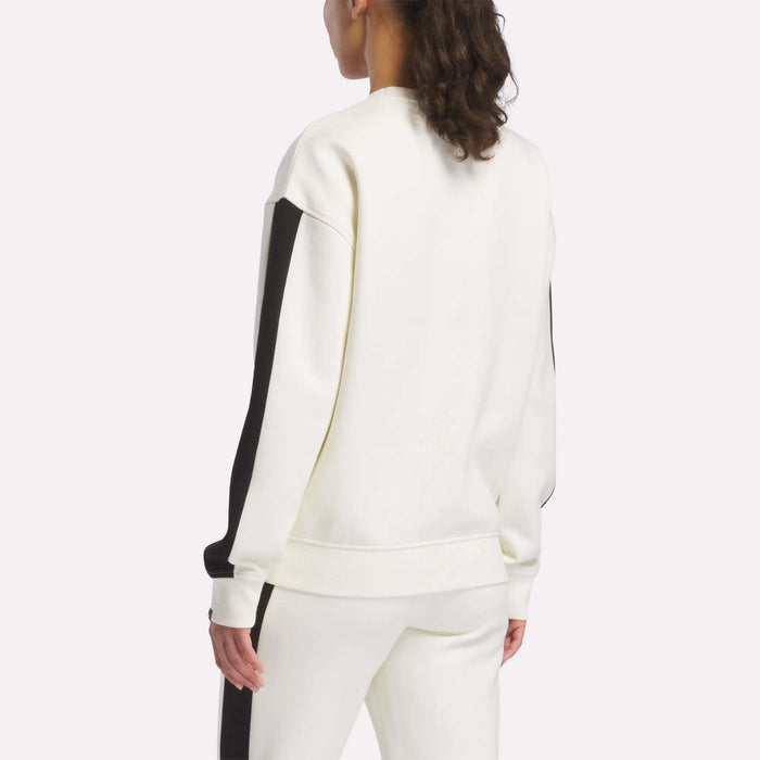 A person is seen from the back wearing a Reebok Women's Fleece Crew Sweatshirt, featuring soft brushback fleece for comfort, paired with matching pants with black stripes against a plain light background.