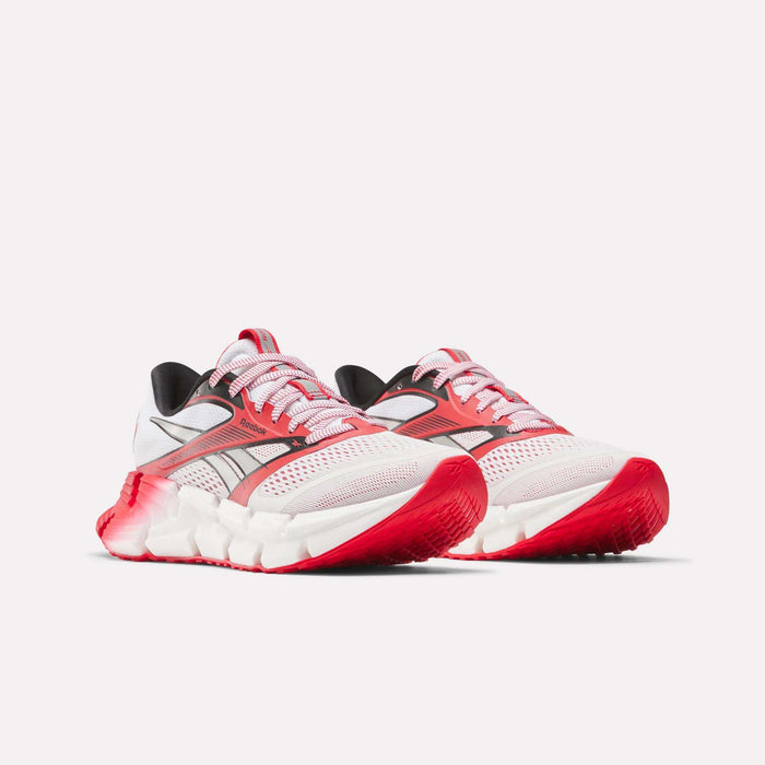 The Reebok Women's FloatZig 2 AHA Running Shoes feature white mesh uppers with red and pink accents, chunky energy-returning white soles, red detailing on the toe and outsole, and are displayed on a plain white background.