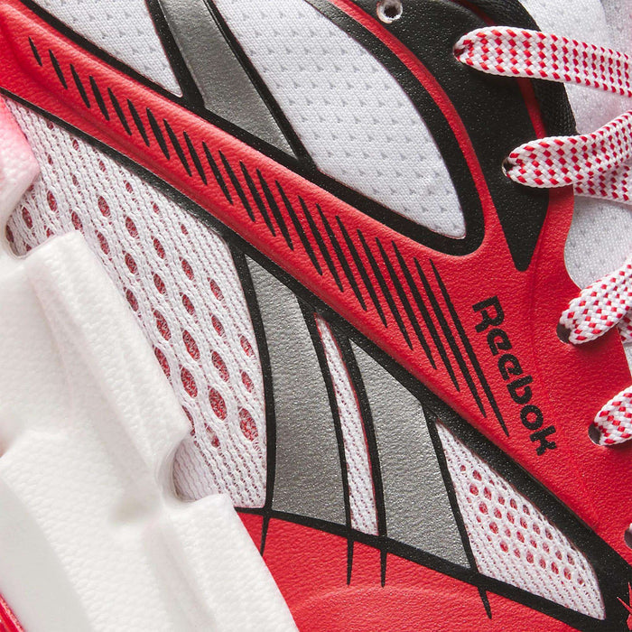 Close-up of a Reebok Women's FloatZig 2 AHA Running Shoe in red, white, and black, featuring textured mesh, bold graphic lines, energy-return cushioning foam midsole, and Reebok branding by the laces.