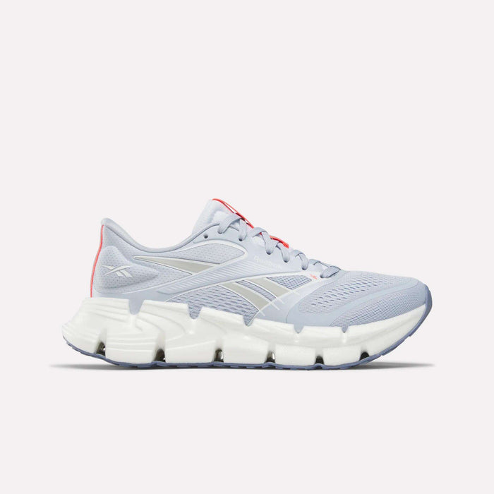 The Reebok Women's FloatZig 2 Running Shoes feature a light gray mesh upper, Superfloat+ cushioning, white segmented sole, silver accents, subtle side logo, and touches of red near the tongue and heel for stylish comfort.