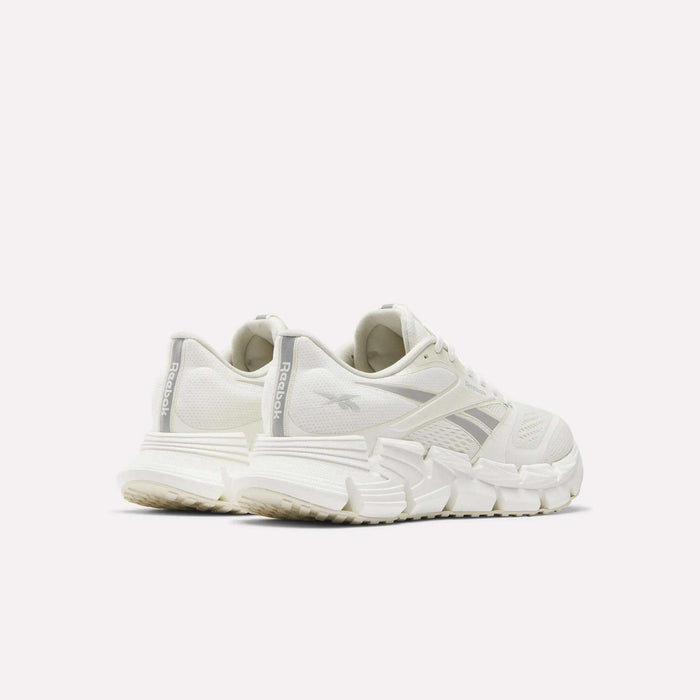 The Reebok Women's FloatZig 2 Running Shoes in white are shown from the back and side against a plain light background, emphasizing the chunky energy-returning cushioning and prominent Reebok branding on the heel and side.