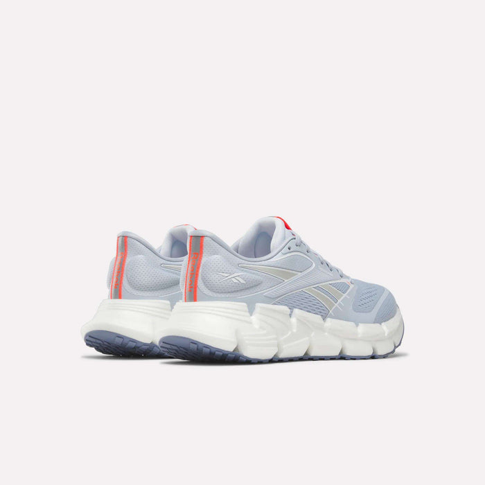 A pair of Reebok Women's FloatZig 2 Running Shoes in light blue with Superfloat+ cushioning, white soles, gray accents, and red-orange heel tabs, displayed rear view on a plain white background.