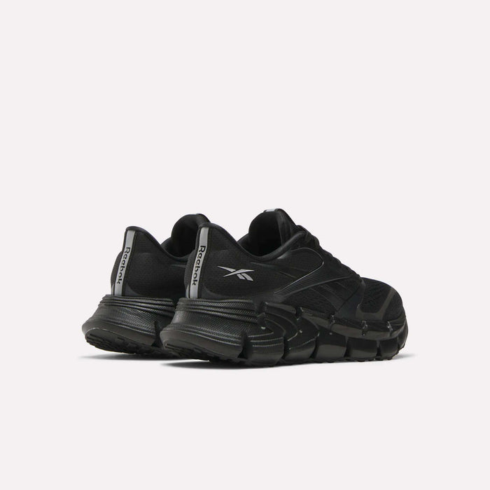 A pair of Women's FloatZig 2 Running Shoes by Reebok in black, with chunky soles and Superfloat+ cushioning, are shown from the back left side. The Reebok logo appears on the heel tabs against a plain light background.