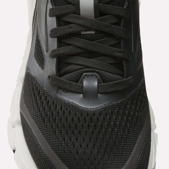 Close-up of the upper part of the Reebok Women's FloatZig 2 Running Shoe in black with mesh fabric, black laces, and gray and white accents on a white sole, featuring Superfloat+ cushioning for comfort.