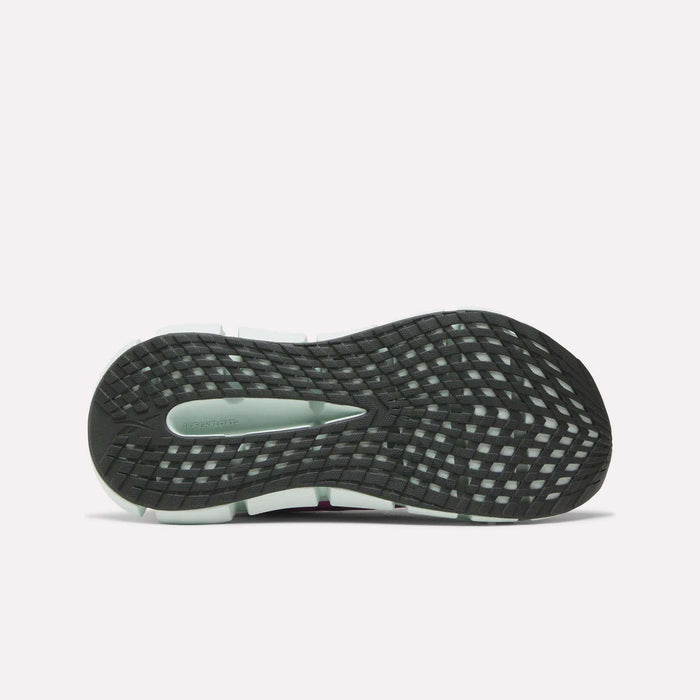 The image displays the bottom of the Reebok Women's FloatZig 2 Running Shoe, featuring a black sole with a grid-like traction pattern, energy-returning cushioning, and a gray section near the heel.