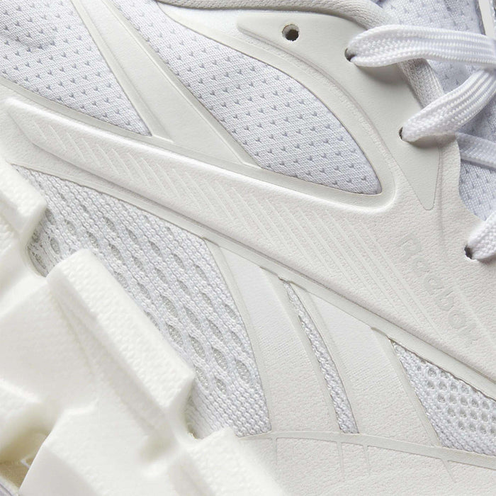 Close-up of Reebok Women's FloatZig 2 Running Shoes in white, showcasing textured mesh, synthetic overlays, intricate stitching, subtle branding, and a chunky sculpted sole with Superfloat+ cushioning.