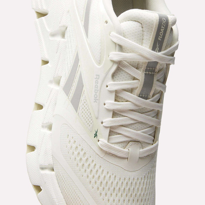 A close-up of the Reebok Women's FloatZig 2 Running Shoes, showing white textured mesh, a thick segmented energy-returning sole, lace-up design, subtle grey accents, and FLOATZIG branding on the tongue.