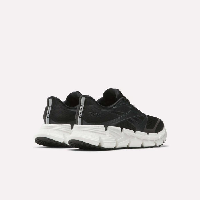 A pair of Reebok Women's FloatZig 2 Running Shoes in black with thick, white segmented soles and Superfloat+ cushioning, displayed from a rear side angle against a plain light background.