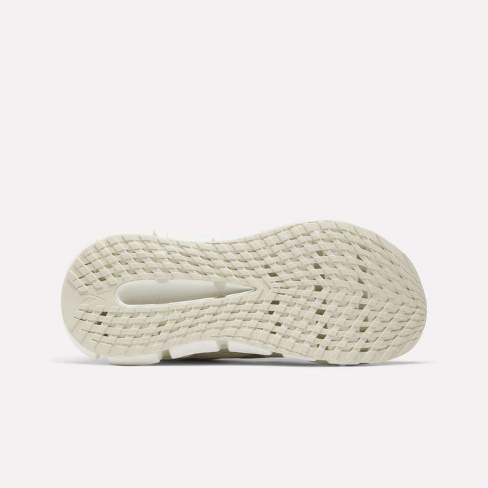 The image displays the bottom view of a white Reebok Women's FloatZig 2 Running Shoe, featuring a grid-like textured tread and energy-returning cushioning, set against a plain white background.
