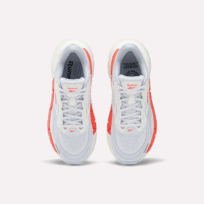Top view of Women's FloatZig Double Running Shoes by Reebok, in white with bright orange side accents and branded tongue, set against a plain light background.