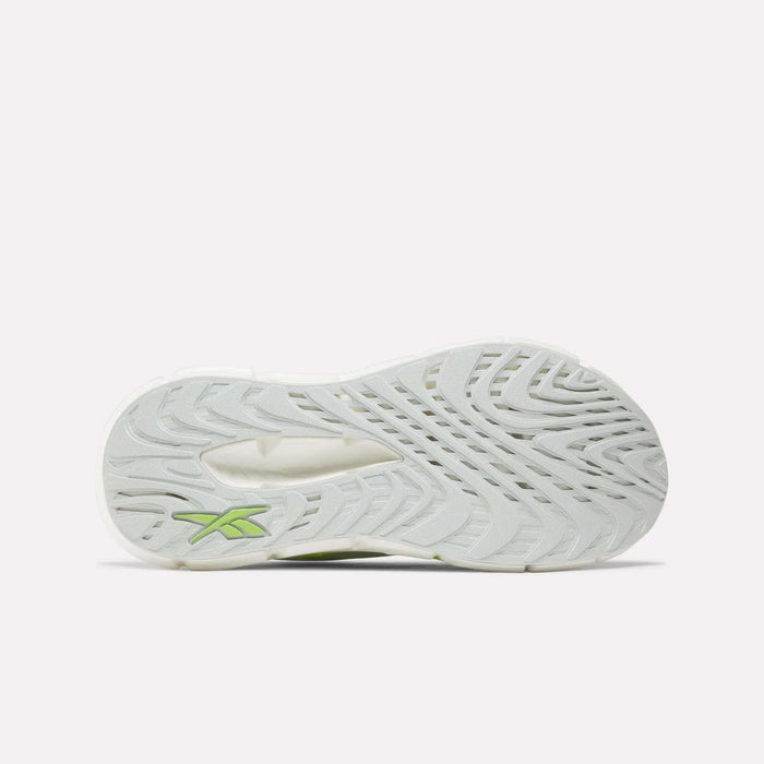 The image shows the bottom of a white Women's FloatZig Double Running Shoe by Reebok, featuring a wavy tread pattern and a small green logo near the heel, designed for maximum cushioning on long runs.