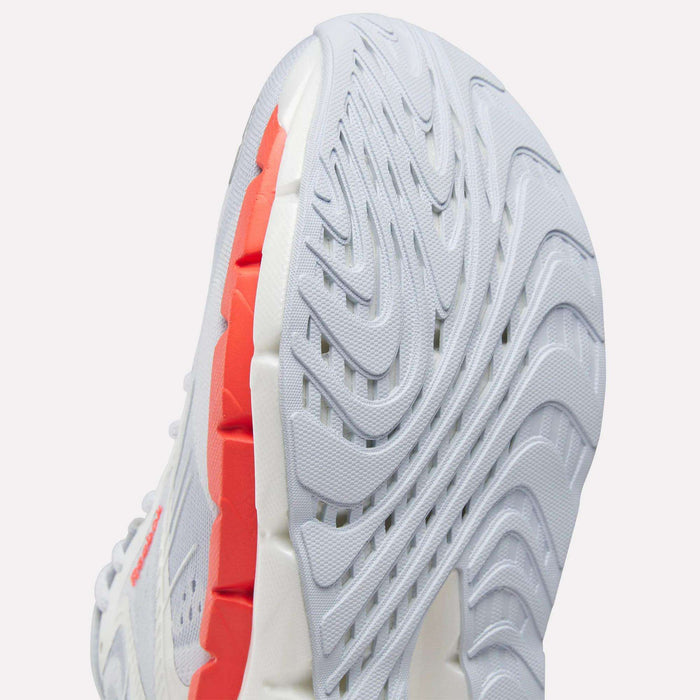 Close-up view of the sole of a Reebok Women's FloatZig Double Running Shoe, featuring white and light gray cushioning, wavy tread patterns, and red accents along the inner edge.