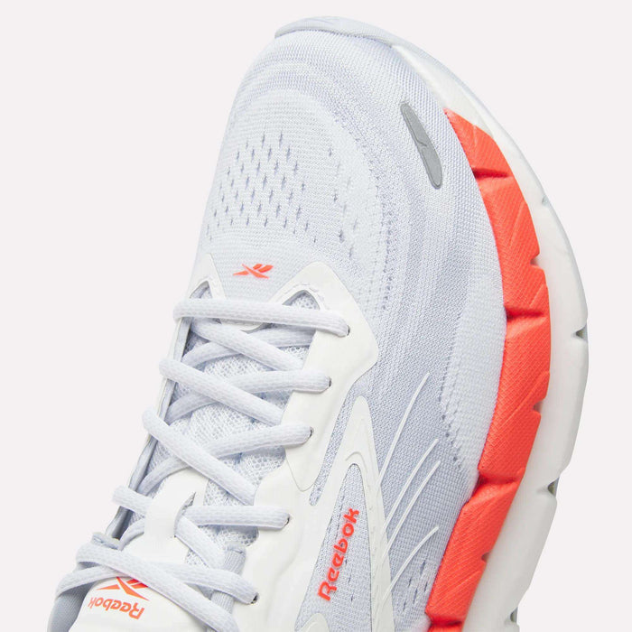 Close-up of light gray Reebok Women's FloatZig Double Running Shoes with white laces, orange midsole accent, mesh texture, and Reebok logos—ideal for max-cushioned miles and all-day comfort.