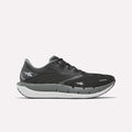 A pair of Reebok Women’s FloatZig Tread Running Shoes in Black/Washed Black/Chalk, featuring a white sole, the Reebok logo on the side and heel, and a breathable mesh upper, is shown from the left against a plain white background.