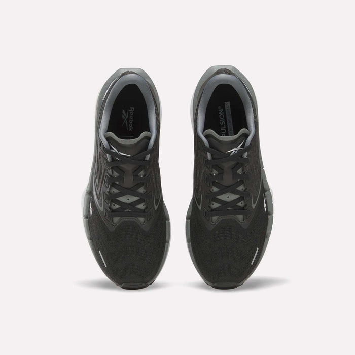 A pair of Women’s FloatZig Tread Running Shoes by Reebok, shown from above to display the black breathable mesh uppers, laces, and Reebok logos on the insoles. The sneakers are set against a plain white background.