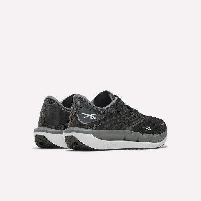 A pair of Reebok Women’s FloatZig Tread Running Shoes in black and gray with white soles, shown from the back and side. These shoes feature a breathable mesh upper and display the Reebok logo on the heel and outer side, making them perfect treadmill running shoes that combine comfort and style.
